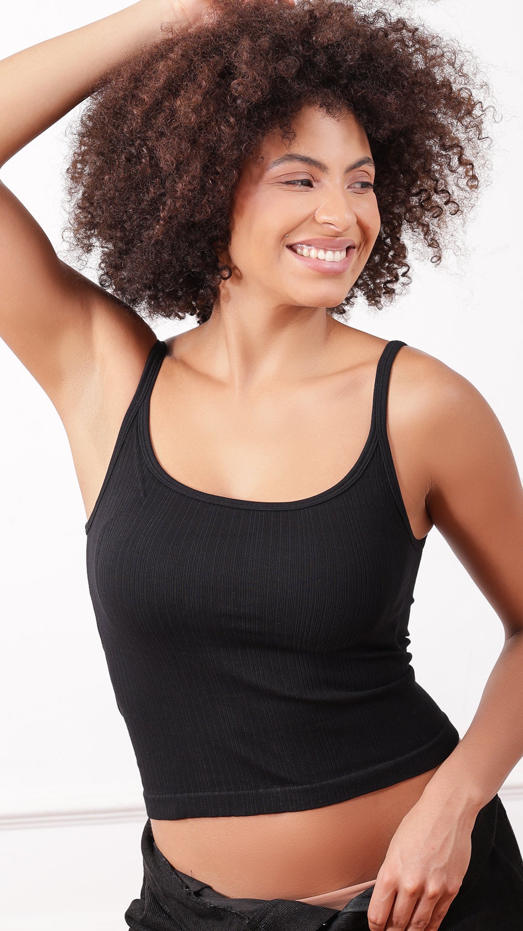 Black ribbed cami top worn with black pants, arms raised
