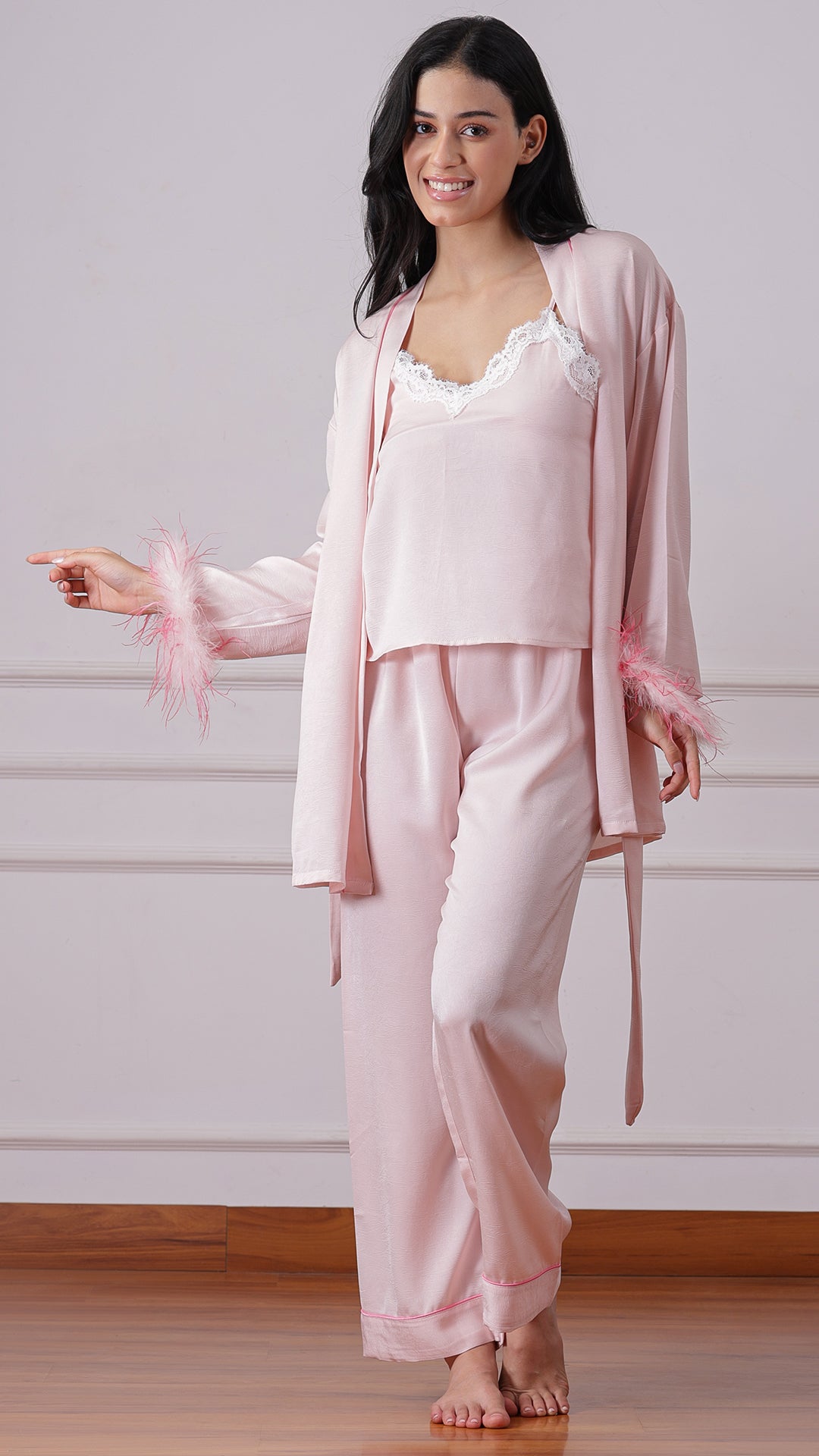 Woman wearing pink satin pajama set with feather-cuff robe