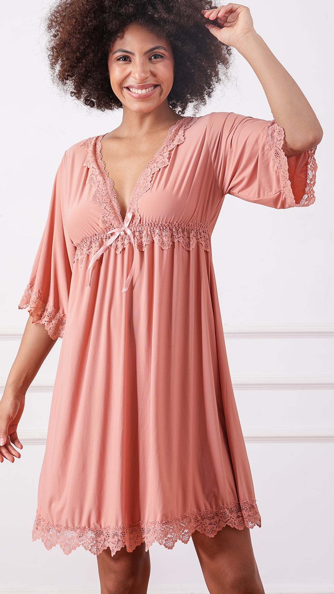 Woman wearing a pink lace-trimmed nightdress with flared sleeves, smiling