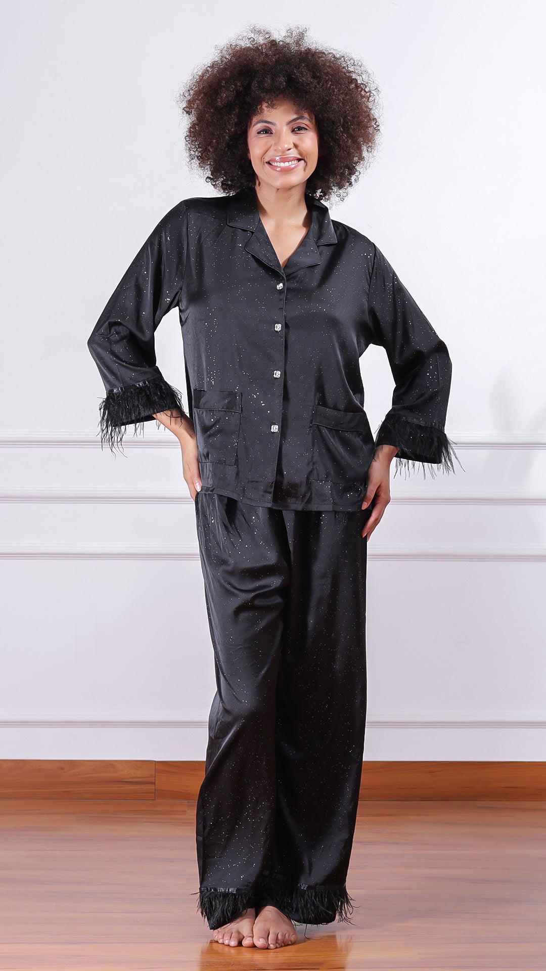 Woman wearing black glitter satin pyjama set with feather-trim cuffs