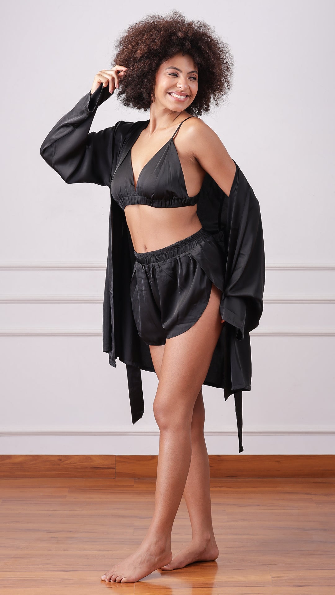 Side view of woman wearing black satin bralette, shorts and robe