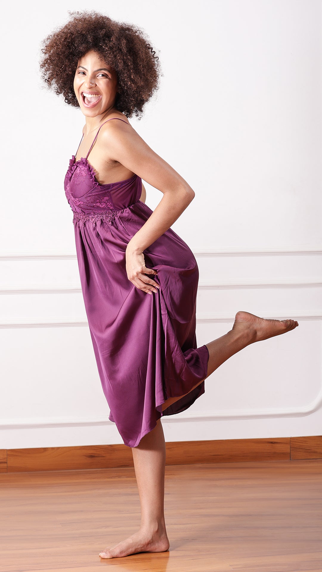Side view of woman wearing purple satin nightgown, kicking leg back