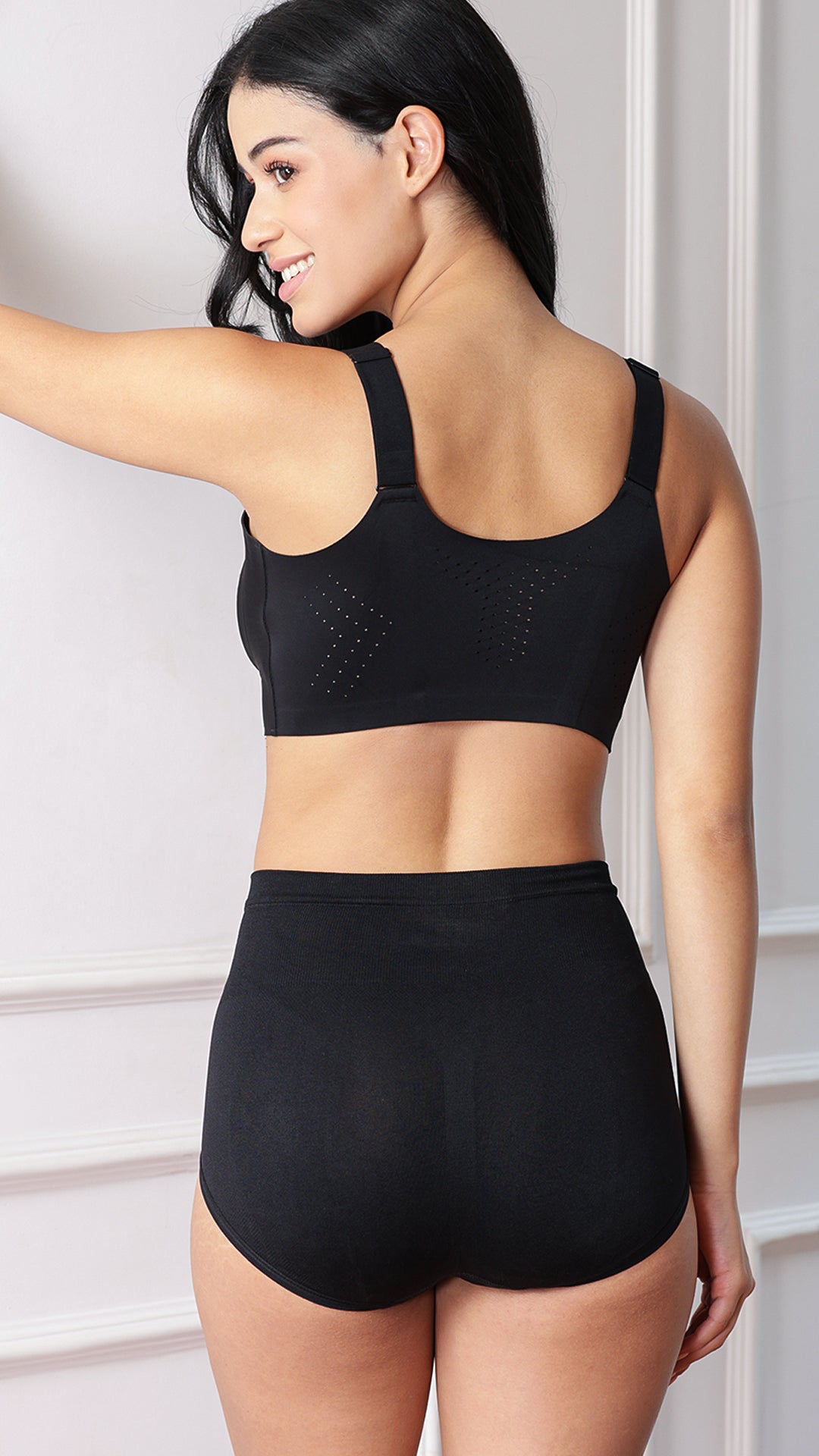 Back view of model wearing black sports bra and briefs showing perforated ventilation