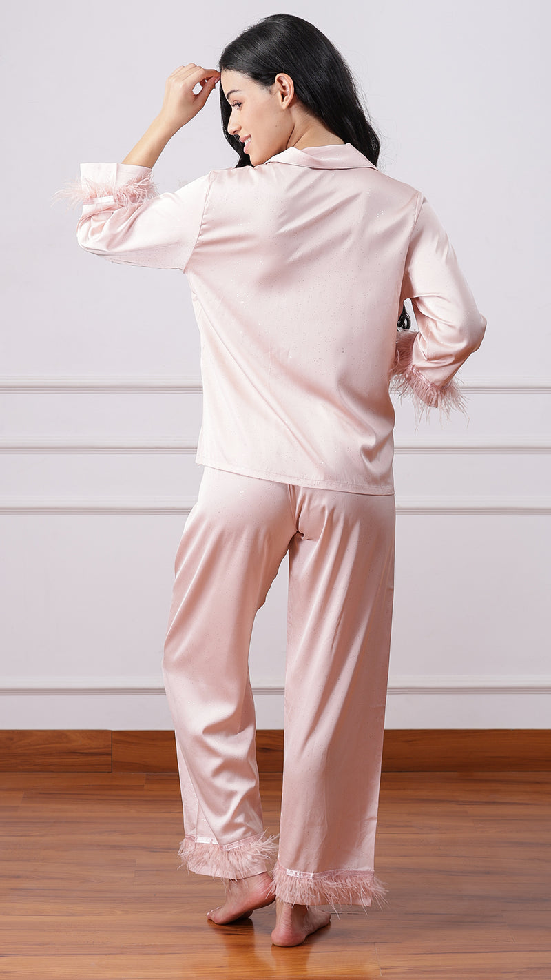 Back view of woman wearing blush pink satin pyjama set with feather cuffs