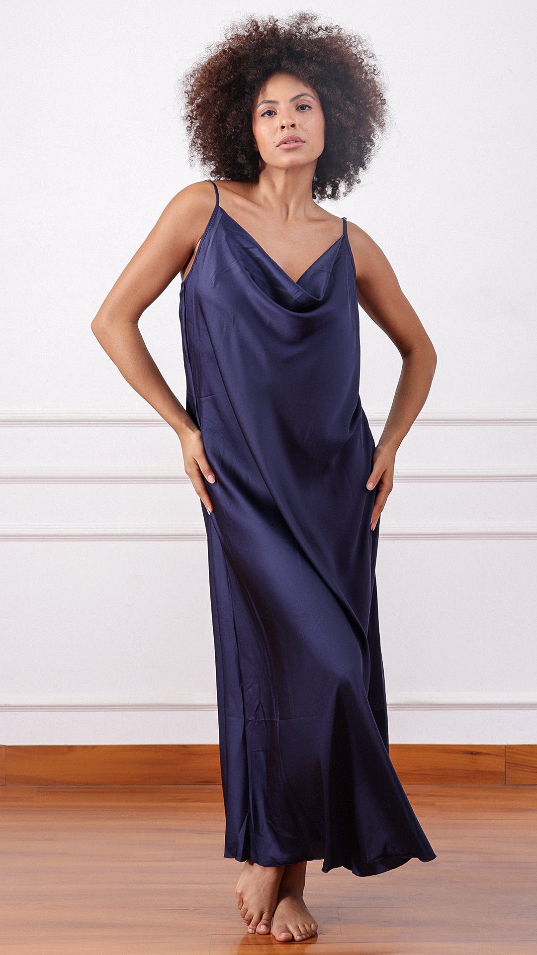Woman wearing a navy satin cowl-neck slip dress, hands on hips