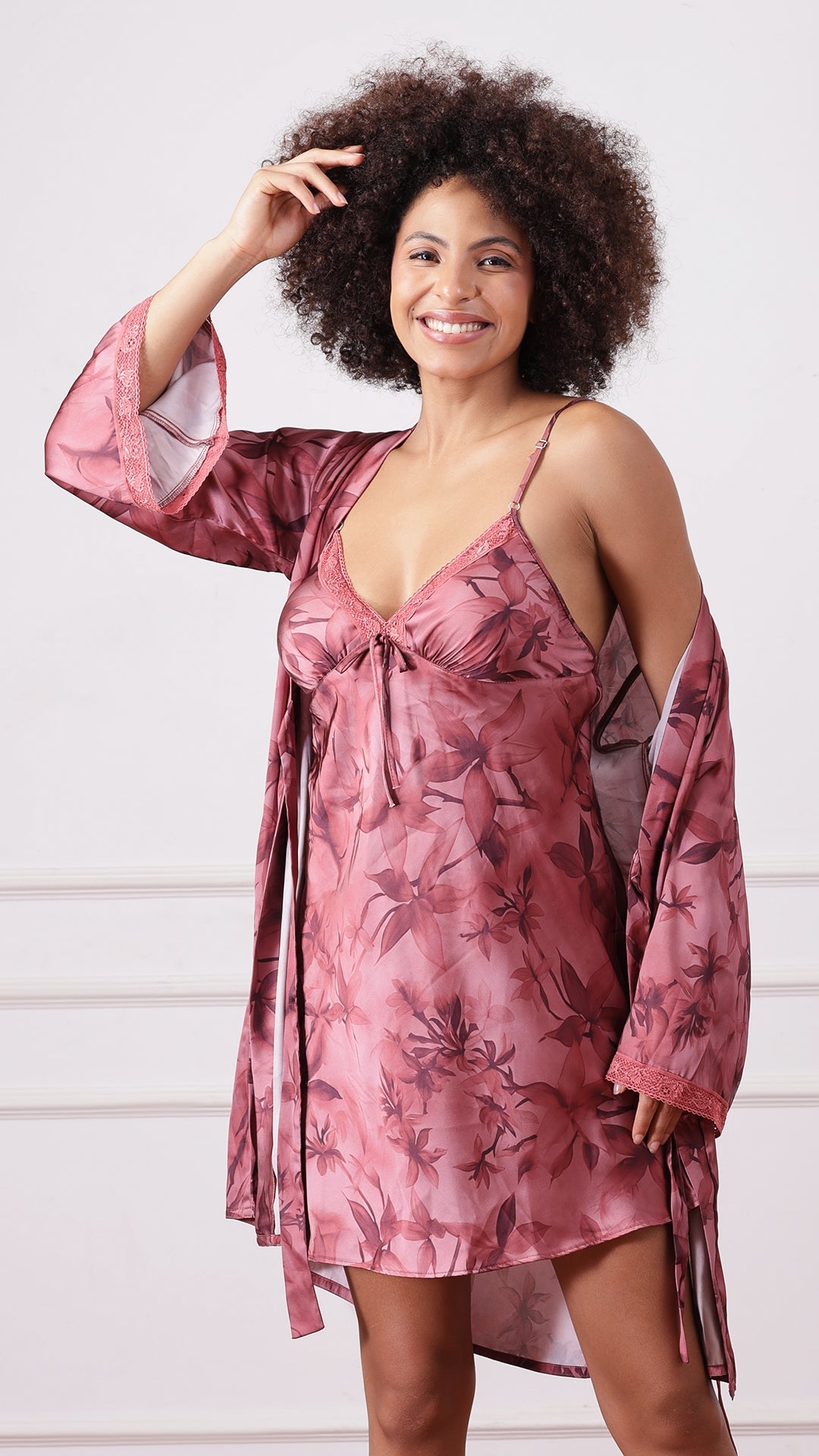 Woman wearing a mauve floral print satin nightdress and matching robe, one hand in hair