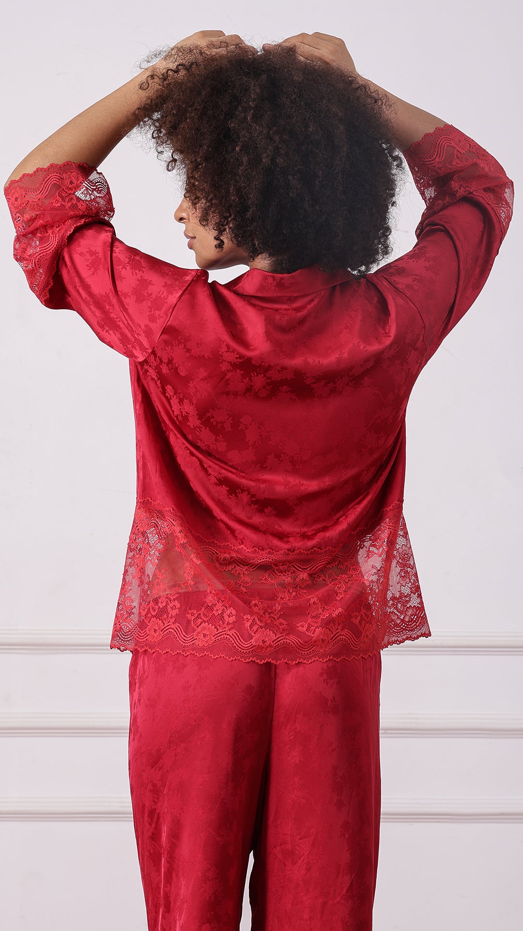 Back view of woman wearing a red satin jacquard pyjama set with lace hem