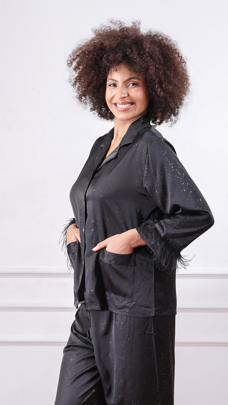 Side view of woman wearing black glitter satin pyjama set, hands in pockets