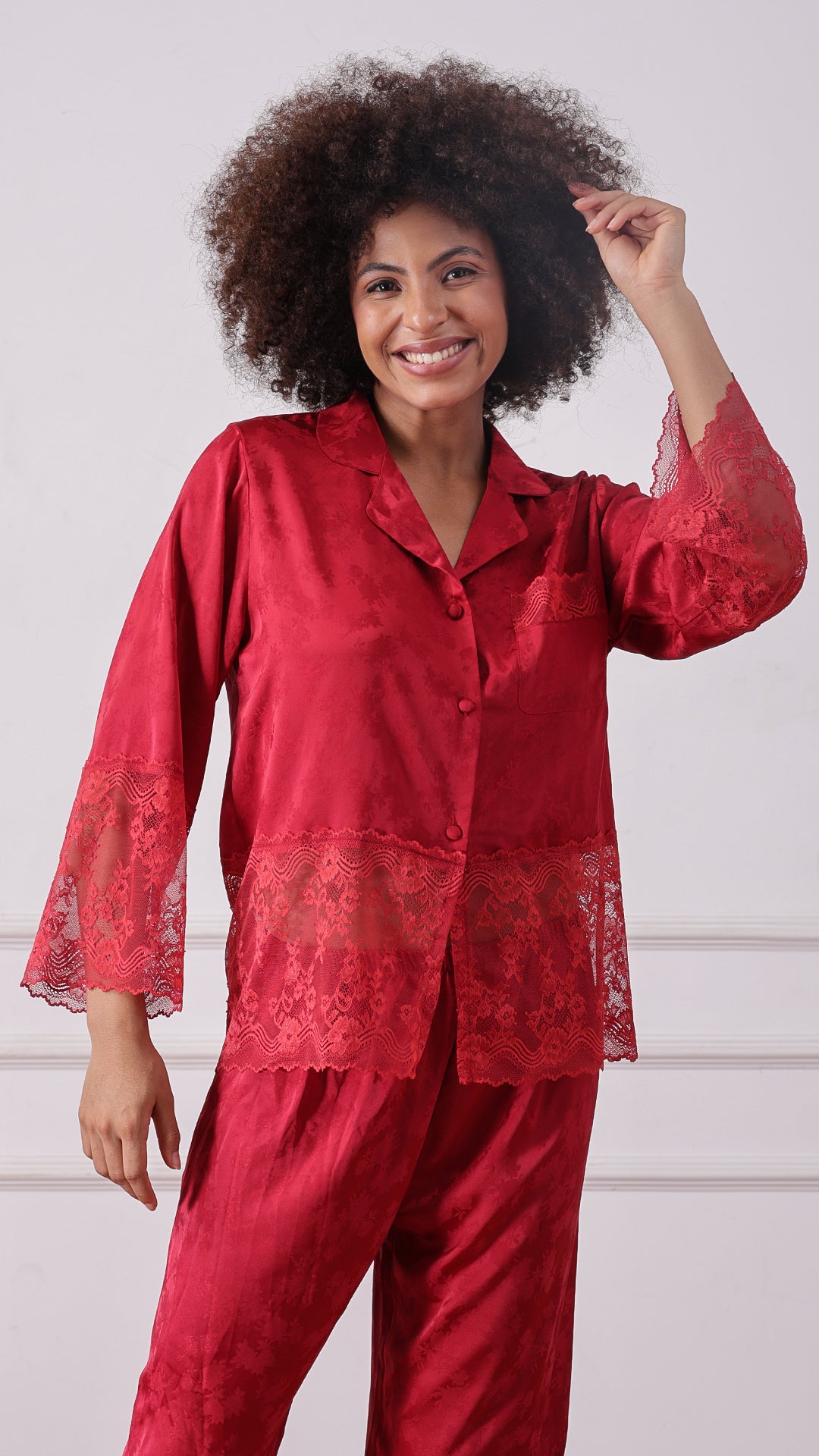 Woman wearing a red satin jacquard pyjama set, smiling with hand on head