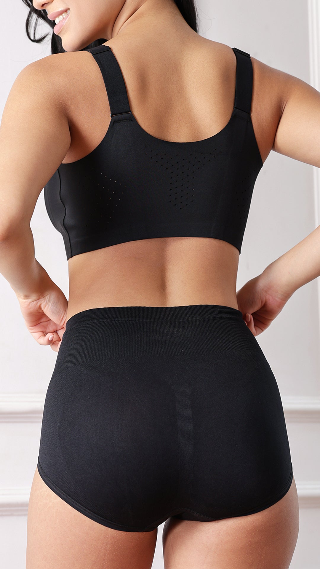 Back view of model wearing black sports bra and high-waist shaper brief