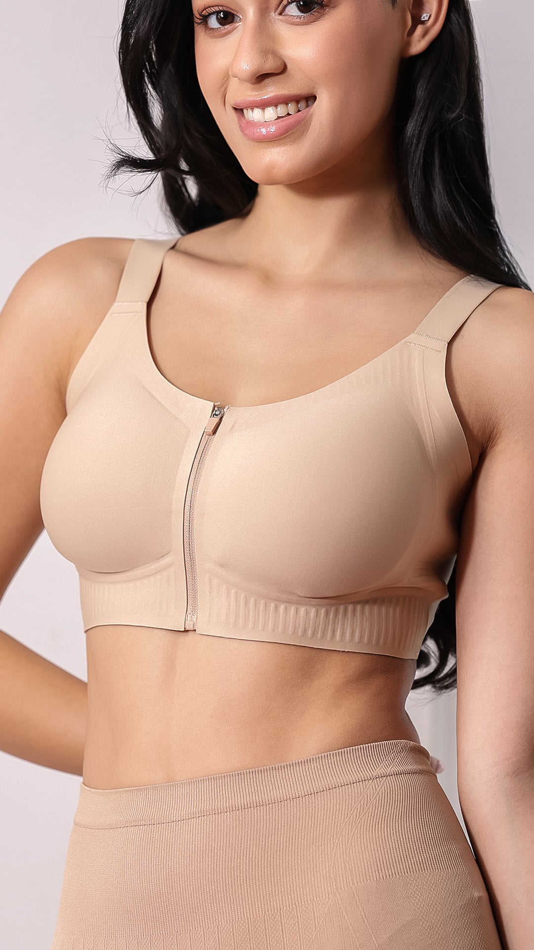 Woman posing in beige front-zip sports bra with embossed cups