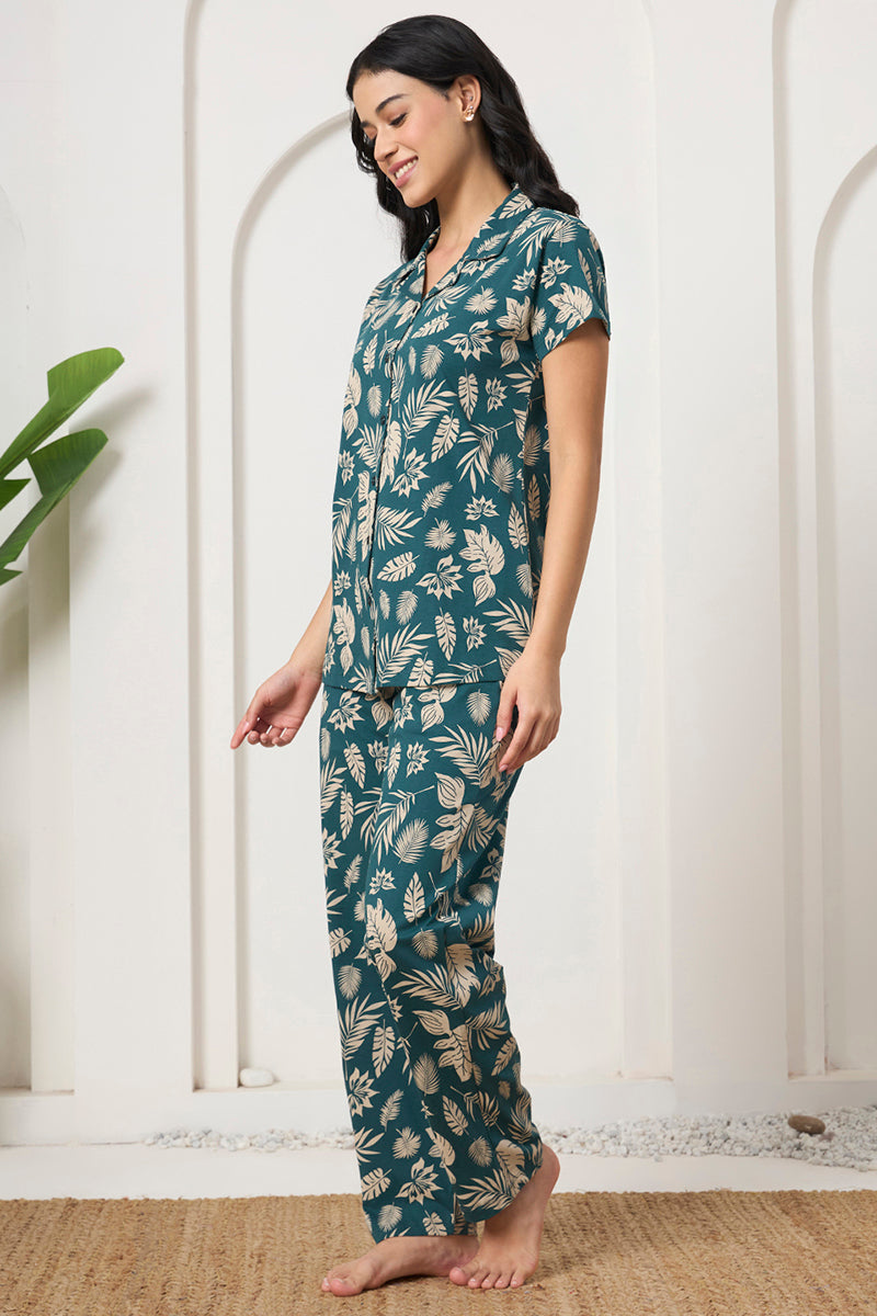 Woman posing in a teal tropical leaf print shirt and pants set, looking down