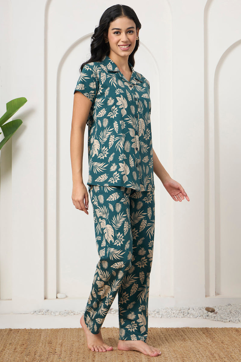 Woman standing in a teal tropical leaf print shirt and pants set, side view