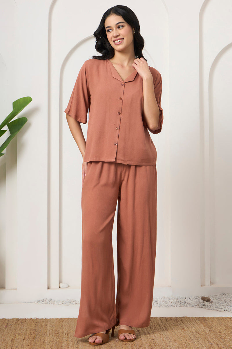 Woman smiling in a rust button down shirt and wide leg pants