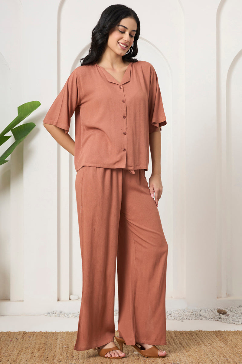 Woman standing in a rust button down shirt and wide leg pants