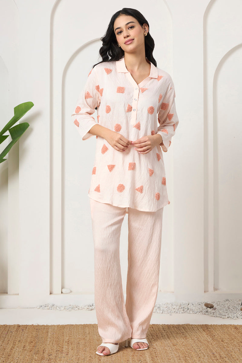 Front pose in a peach embroidered collared tunic and matching pants set against an arched backdrop