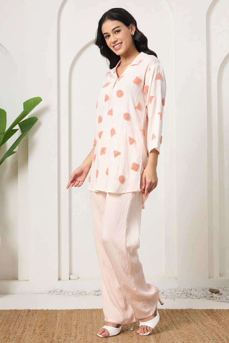 Side view of the peach textured tunic and pant co-ord set styled with white heels