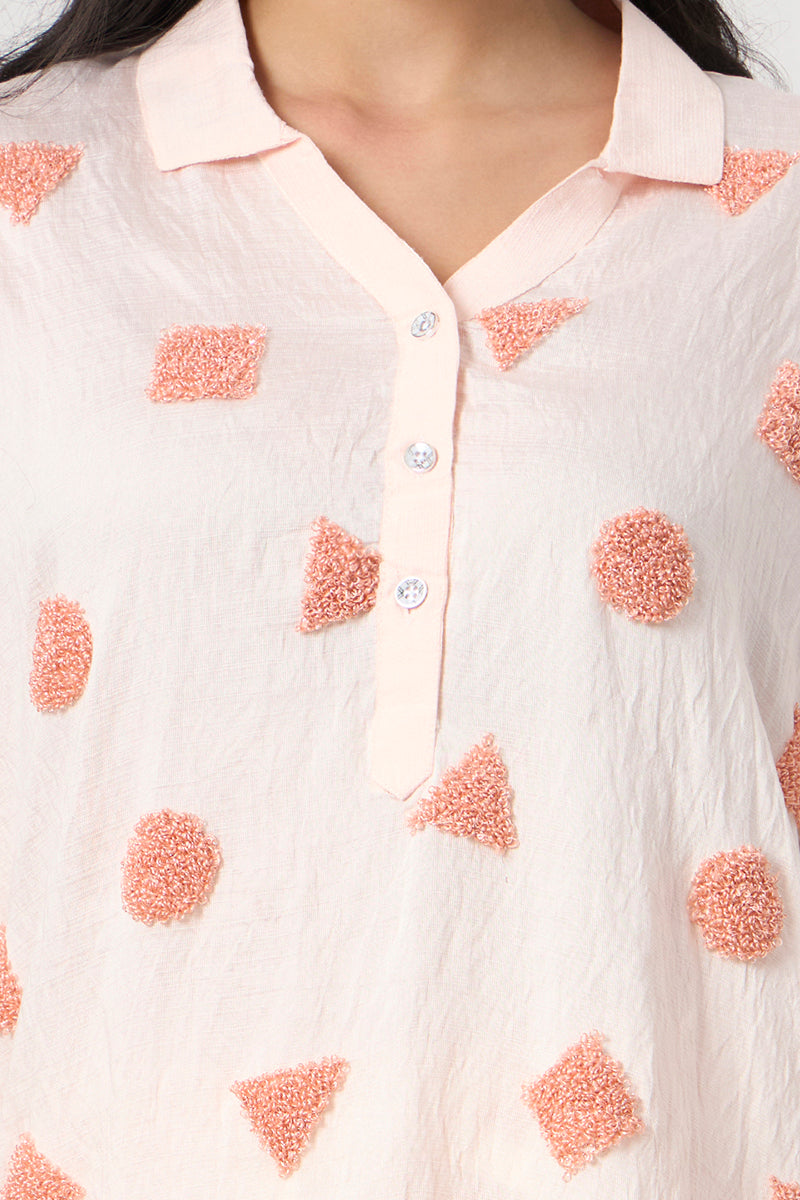 Close-up of the collar and button placket on the peach tunic highlighting the textured embroidered motifs