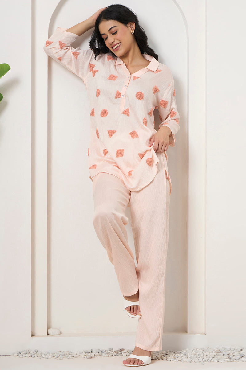 Woman leaning against a wall in a relaxed peach tunic and pant co-ord with textured motif detailing