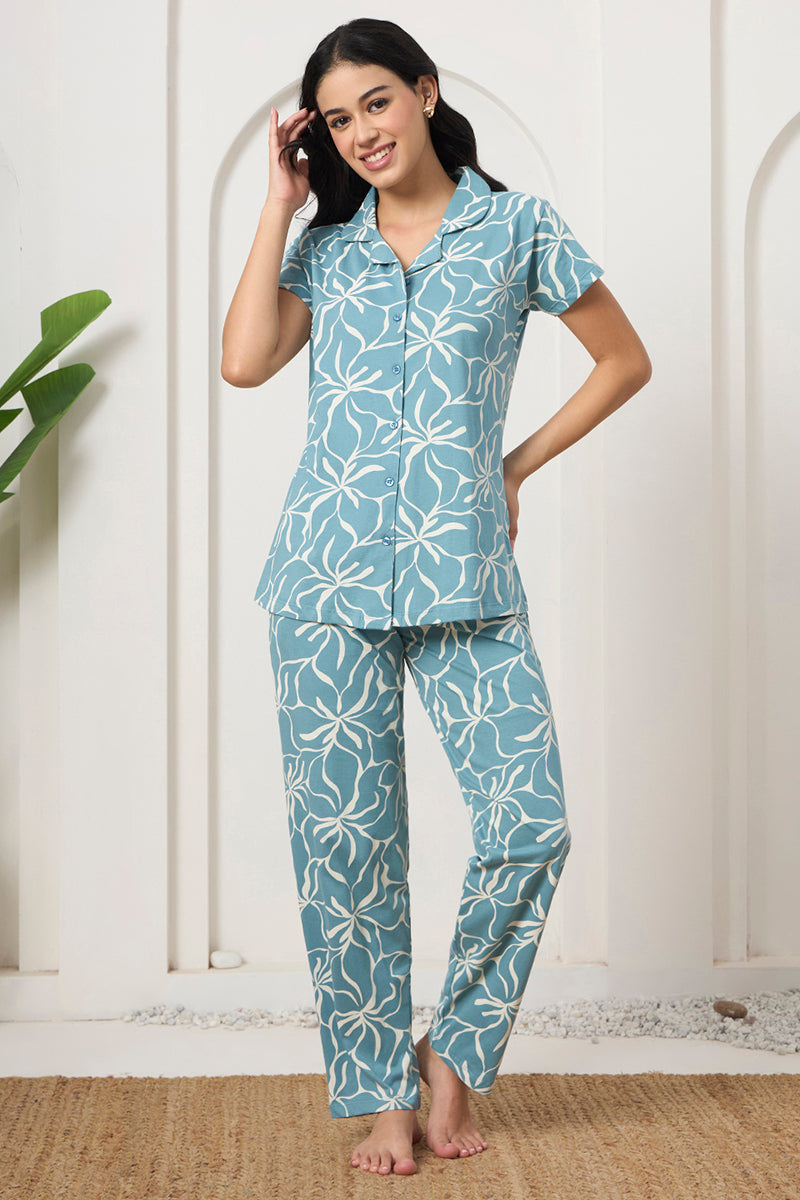 Woman smiling with hand in hair, wearing a dusty blue floral print shirt and pants