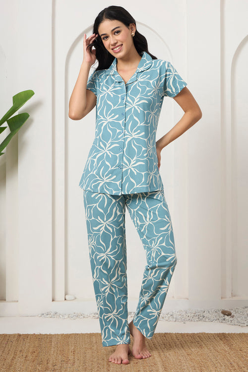 Woman smiling with hand in hair, wearing a dusty blue floral print shirt and pants