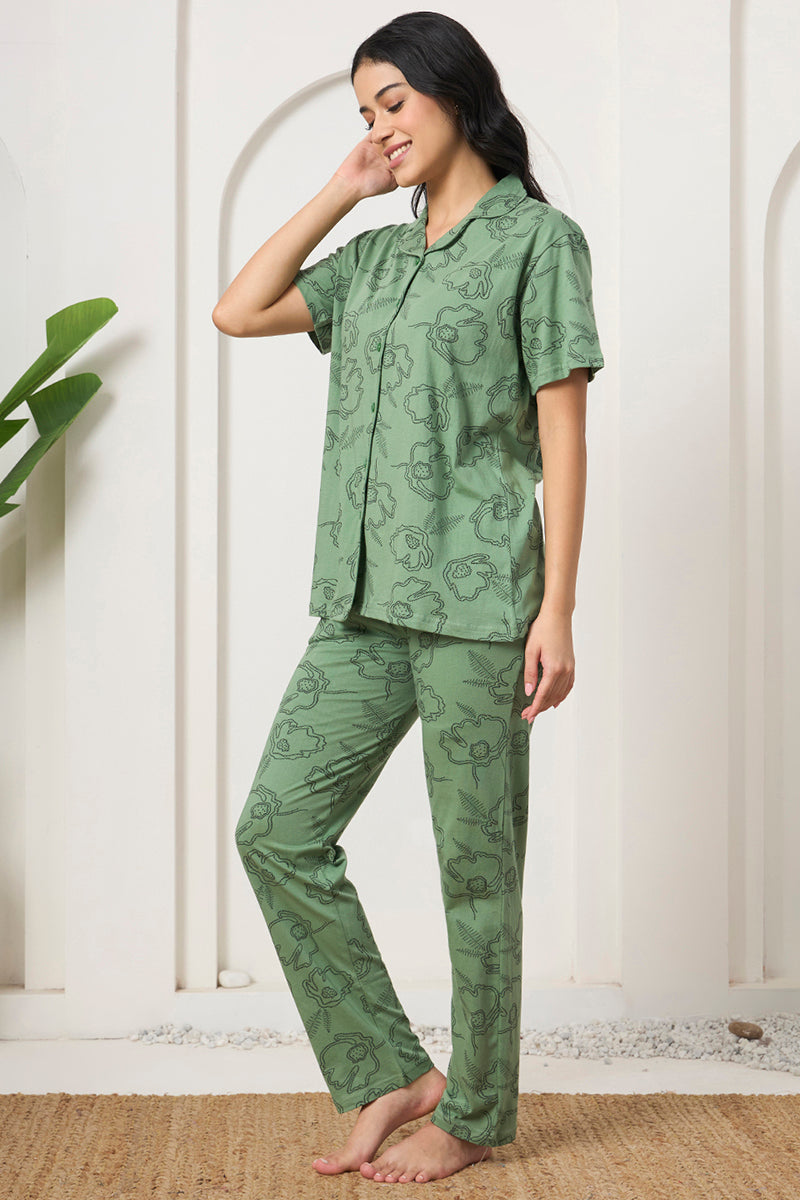 Woman smiling in a sage green floral print shirt and pants, hand in hair
