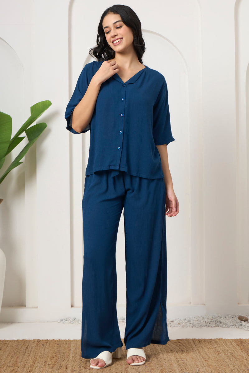 Woman smiling in a teal button down shirt and wide leg pants