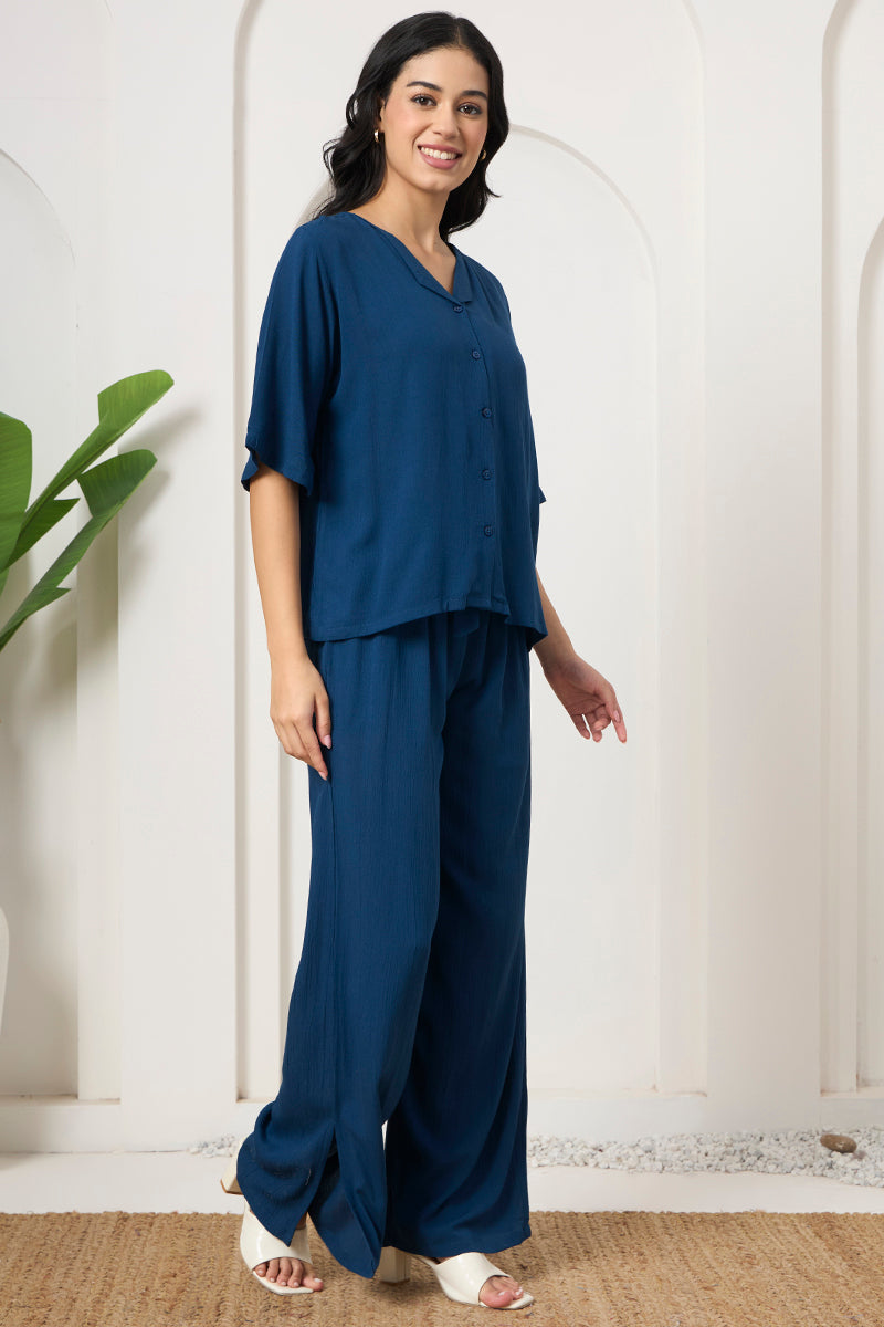 Woman standing in a teal button down shirt and wide leg pants