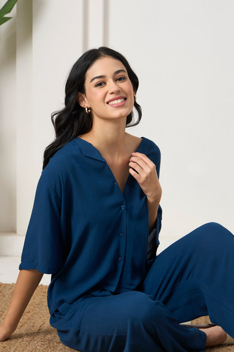 Woman sitting on a jute rug in a teal button down shirt and pants