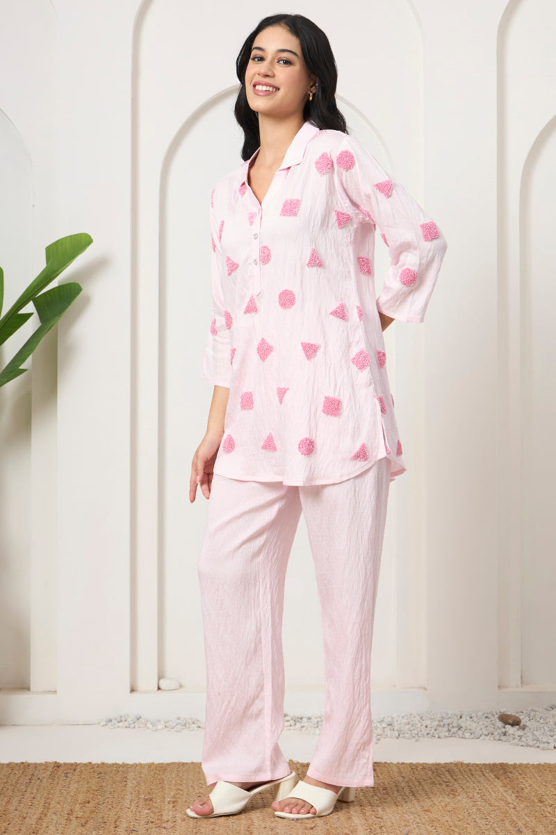 Side pose in a pink embroidered collared tunic and matching pants set against an arched backdrop