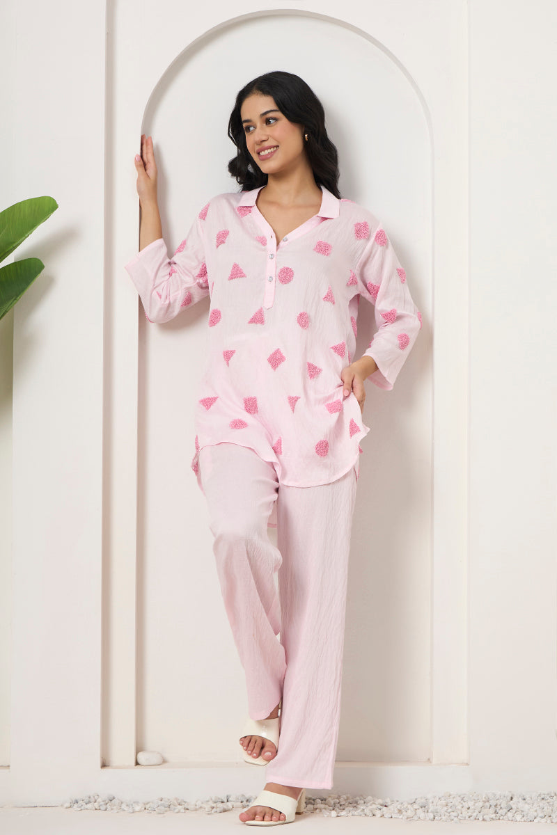 Woman leaning against an arch in a pink textured tunic and pant co-ord set with white heels