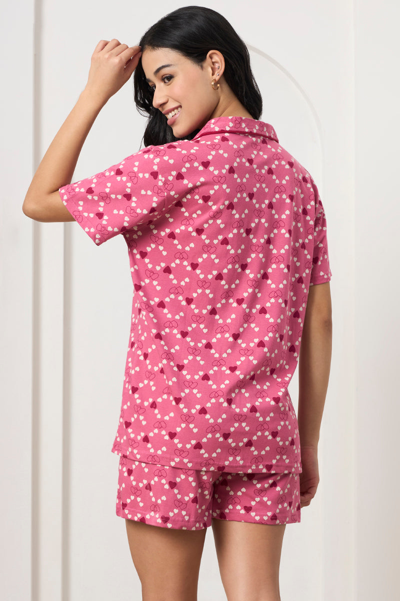 Back view of a woman wearing a pink heart print shirt and shorts, hand in hair