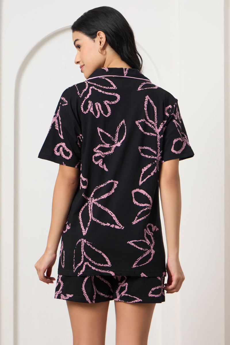 Back view of a woman wearing a black and pink leaf print shirt and shorts