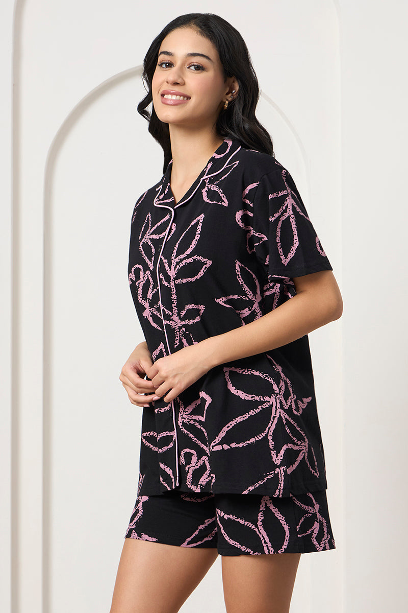 Woman standing in a black and pink leaf print shirt and shorts set, side view