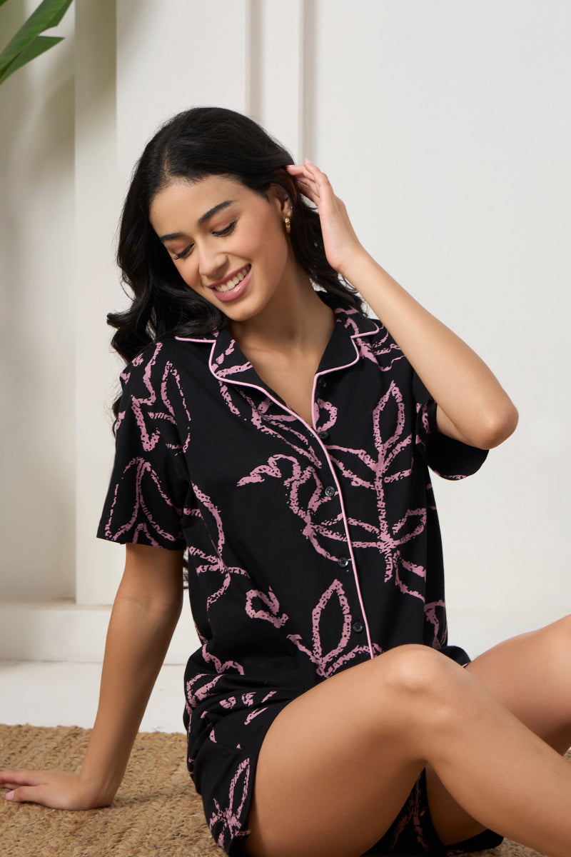 Woman sitting in a black and pink leaf print shirt and shorts set, smiling