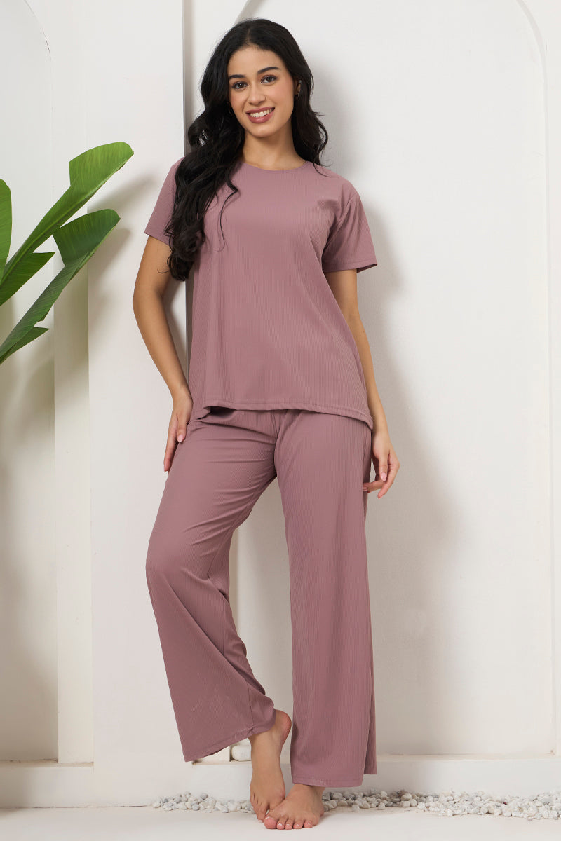 Woman smiling in a mauve ribbed pyjama set against a wall
