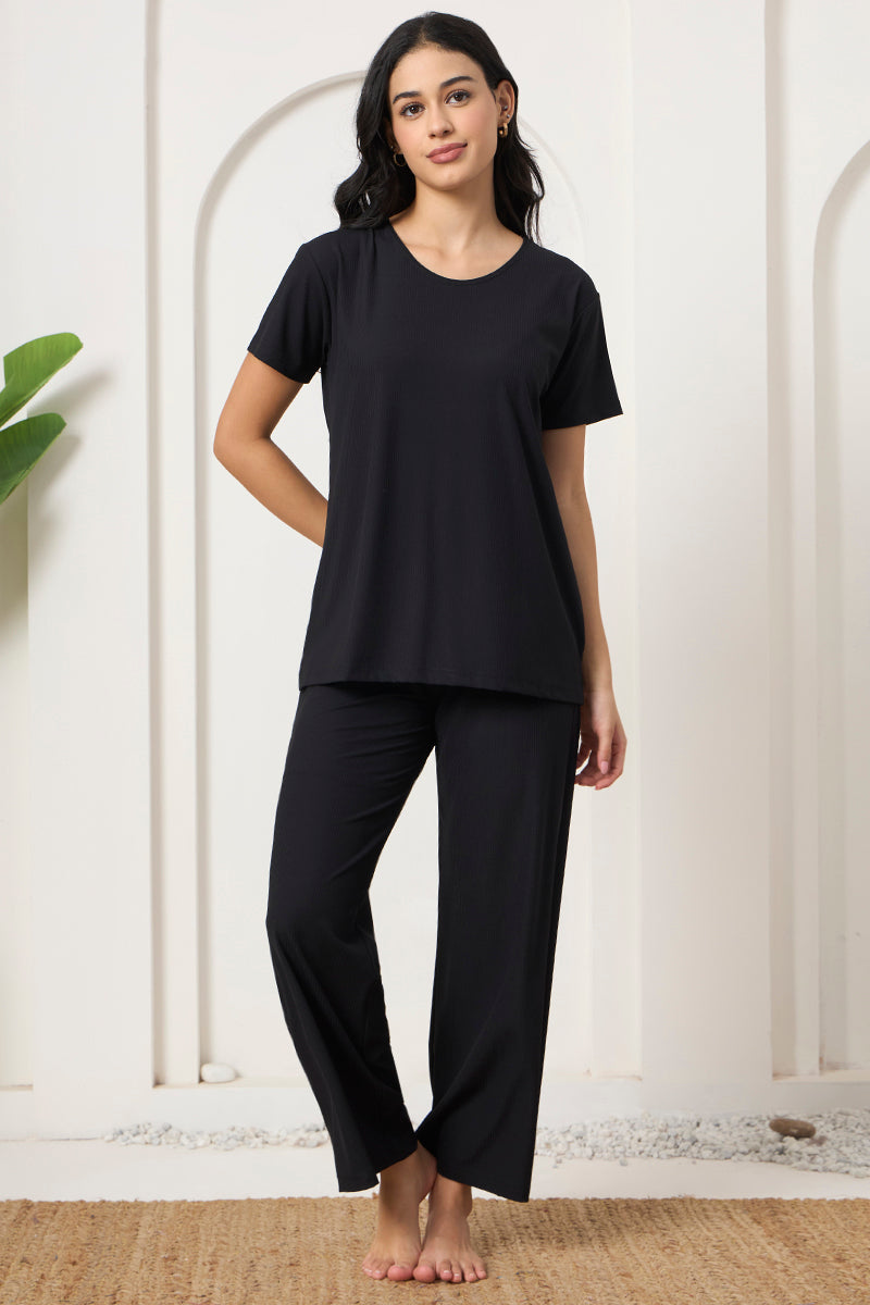 Woman smiling in a black ribbed pyjama set on a jute rug