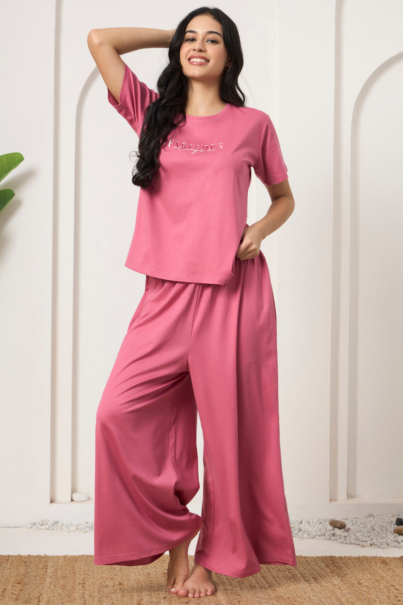 Woman smiling with hand in hair wearing a pink t-shirt and pants set