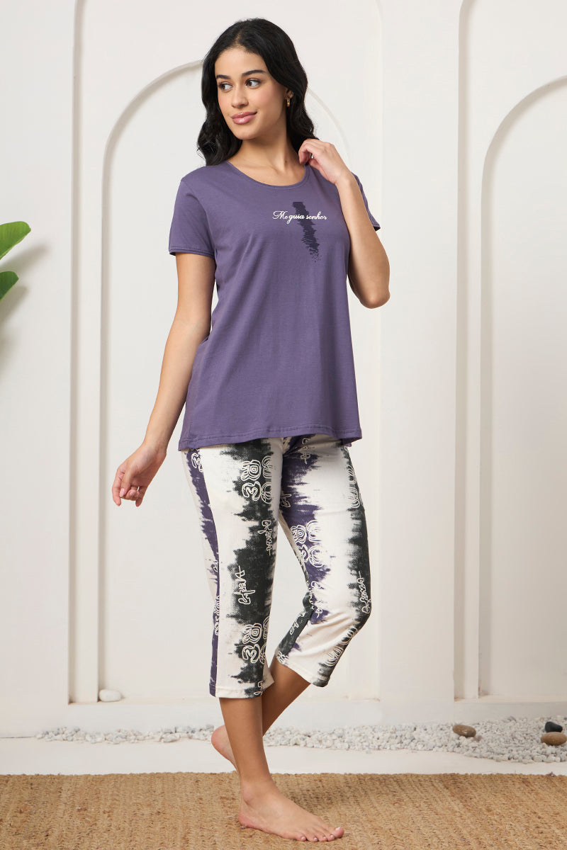 Woman standing in a purple tee and tie-dye print capri pants